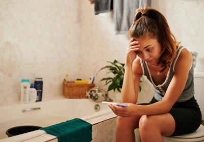 a young distraught woman views her at-home pregnancy test results