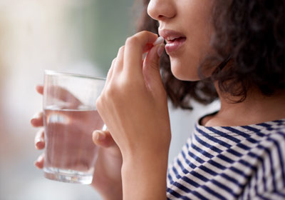 a woman taking an emergency contraceptive tablet with water