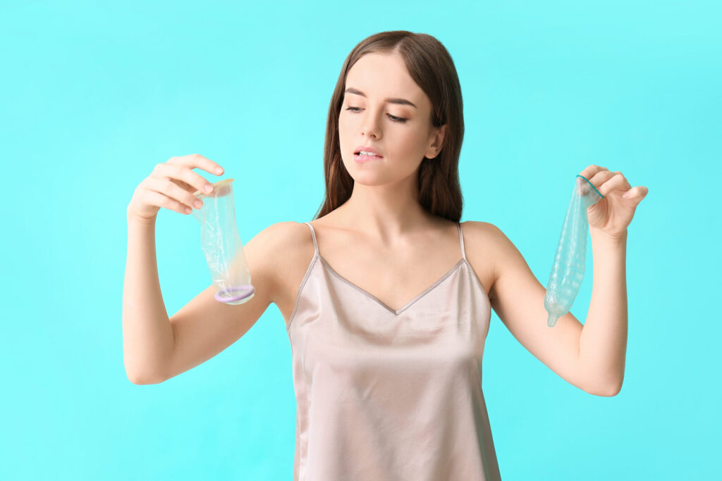 Young woman with male and female condoms on color background