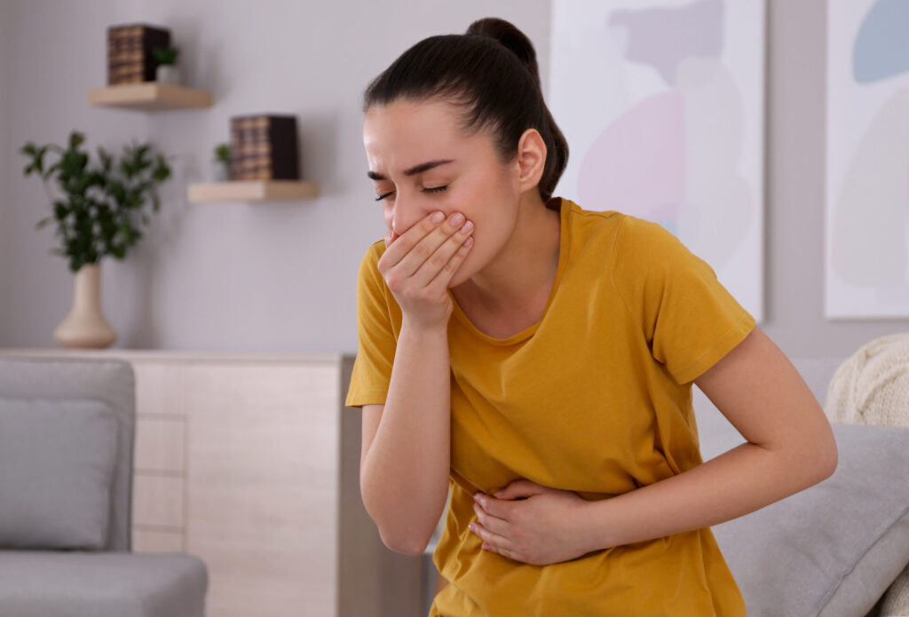 Nauseated woman holding her stomach with one hand and covering her mouth with the other