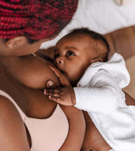 Young African American woman breastfeeding her baby in her bedroom.