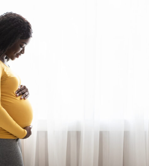 Beautiful pregnant black woman hugging her tummy and enjoying her pregnancy.