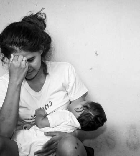 Black and white image of a mom holding her baby, but hanging her head in sadness because of postpartum depression