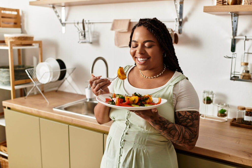 A young African-American woman happily savoring a colorful salad at home for lunch.