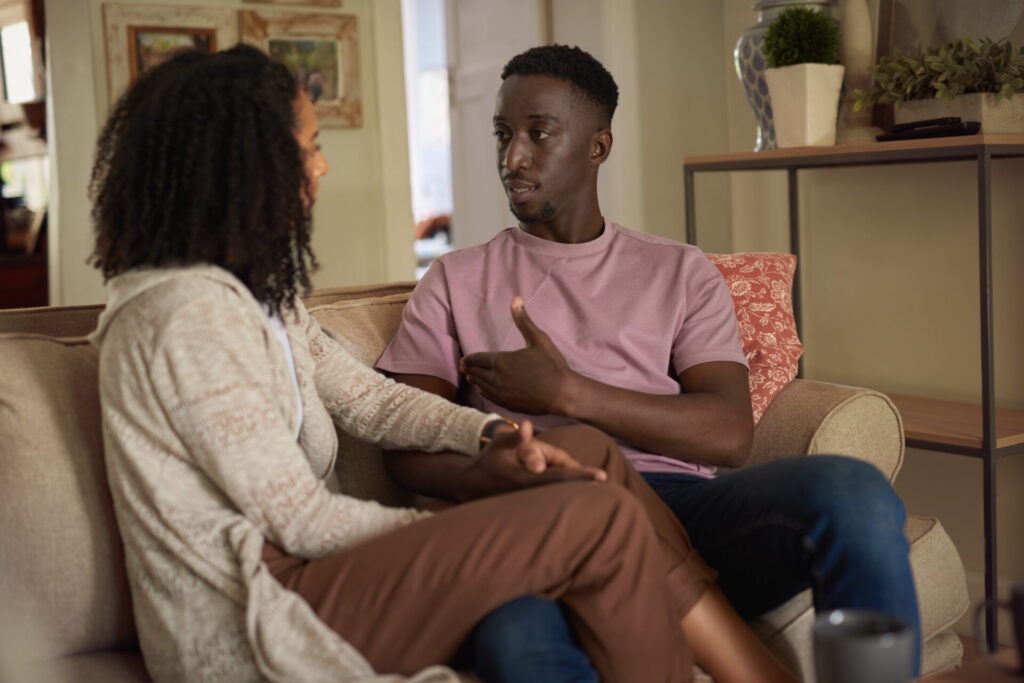 Young multiracial couple having a respectful conversation about STI status while sitting together on their living room sofa at home.