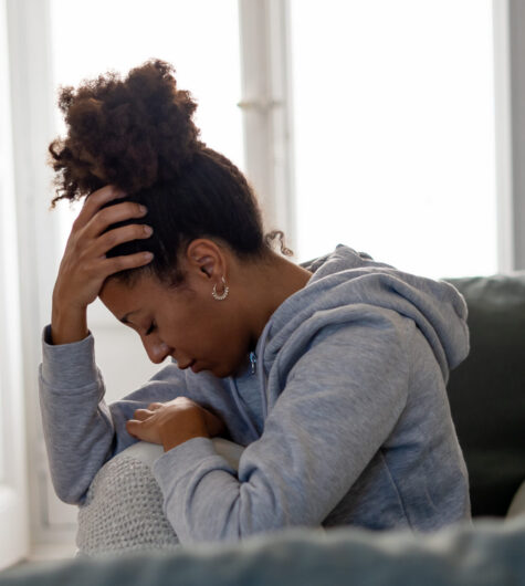 Black woman on her couch worrying, indicating stress about how much she has bled since her abortion